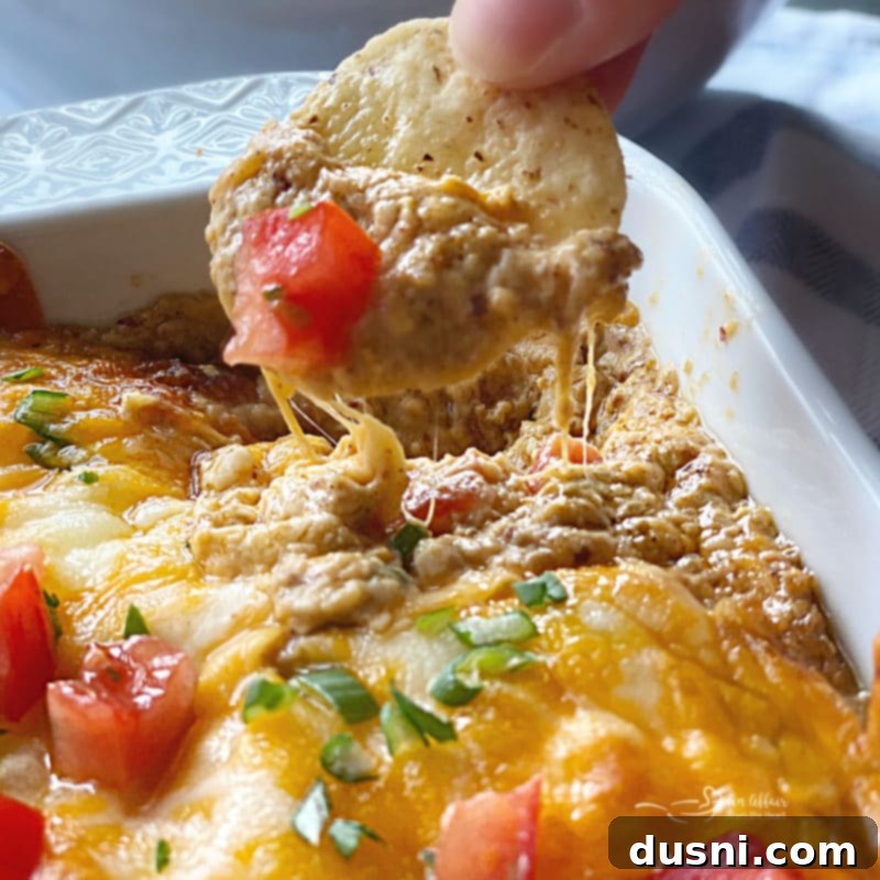 Hot Taco Five Bean Dip with a spoon, topped with tomatoes and green onions.