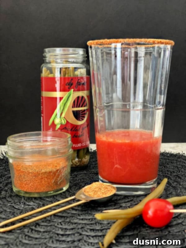 Tomato juice being poured into a spice-rimmed beer glass, starting the preparation of a Kicked Up Red Beer.