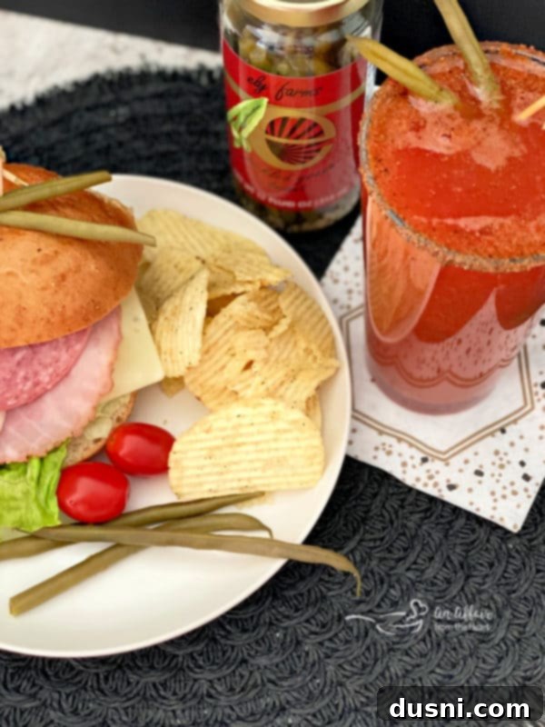 A Kicked Up Red Beer sitting next to a glass jar of Ely Farms pickled green beans, emphasizing the natural, wholesome garnish.