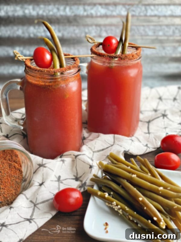 Two Kicked Up Red Beers, garnished with pickled green beans, sitting on a wooden surface, highlighting the vibrant color and appetizing presentation.
