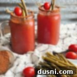 Kicked Up Red Beer with spicy rim and pickled green bean garnish, showcasing a refreshing and flavorful drink.