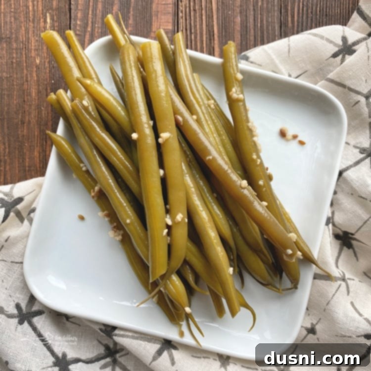 A glass jar filled with fresh Ely Farms Pickled Green Beans, ready to be used as a delicious garnish or snack.