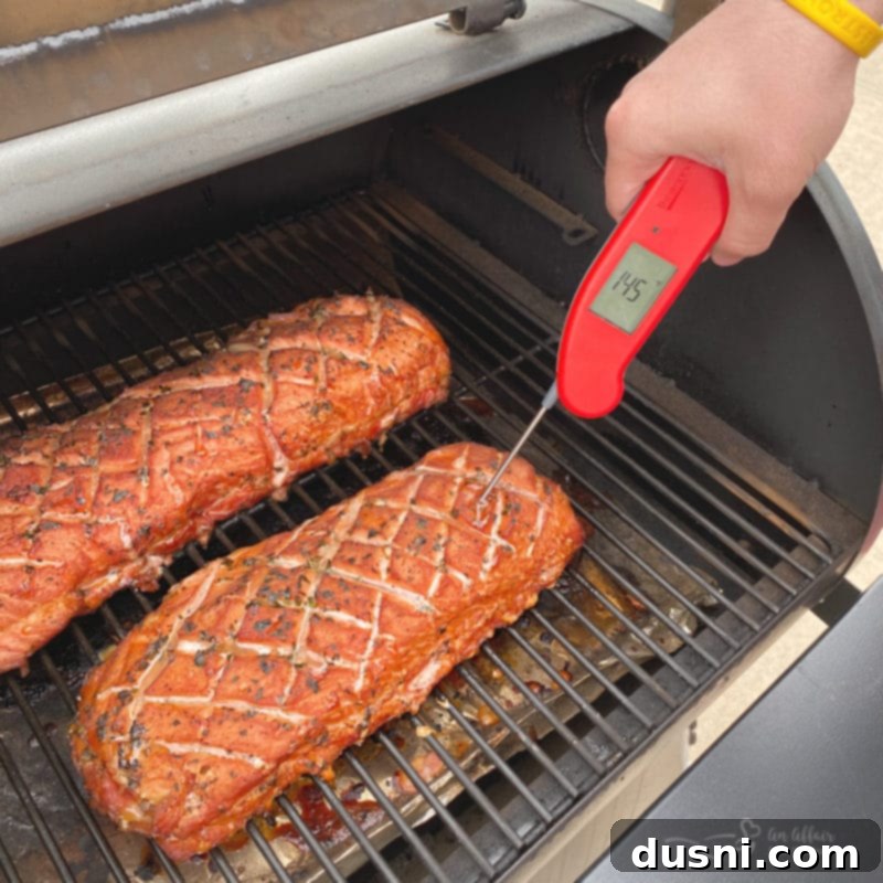 pork loin on grill checking temperature with a thermometer