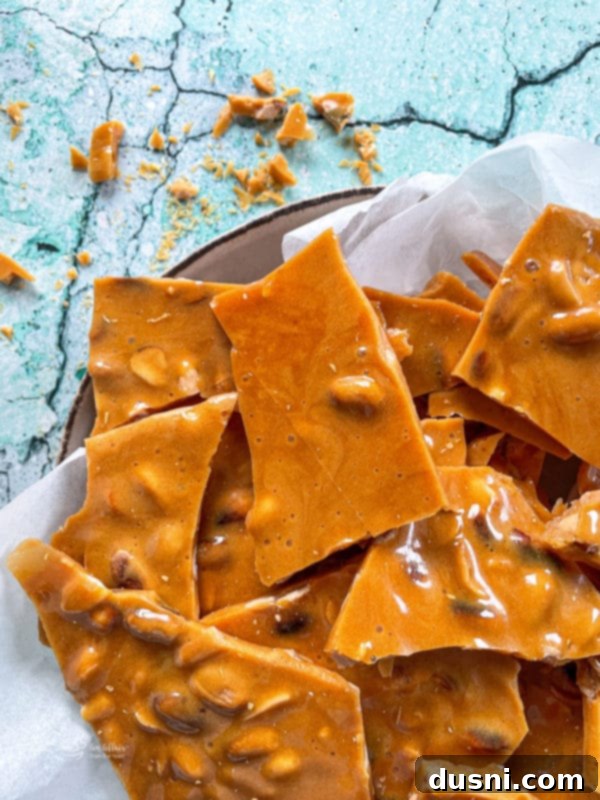 Delicious homemade peanut brittle pieces scattered on a surface, showcasing its golden, crunchy texture with visible peanuts