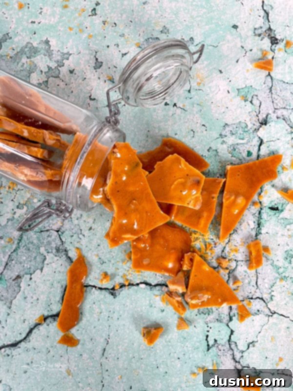 A close-up shot of perfectly golden, crunchy peanut brittle with visible peanuts on a marble surface