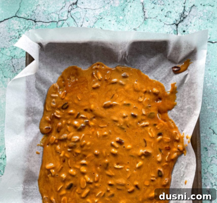 Pouring hot, foamy peanut brittle mixture onto a parchment-lined baking sheet