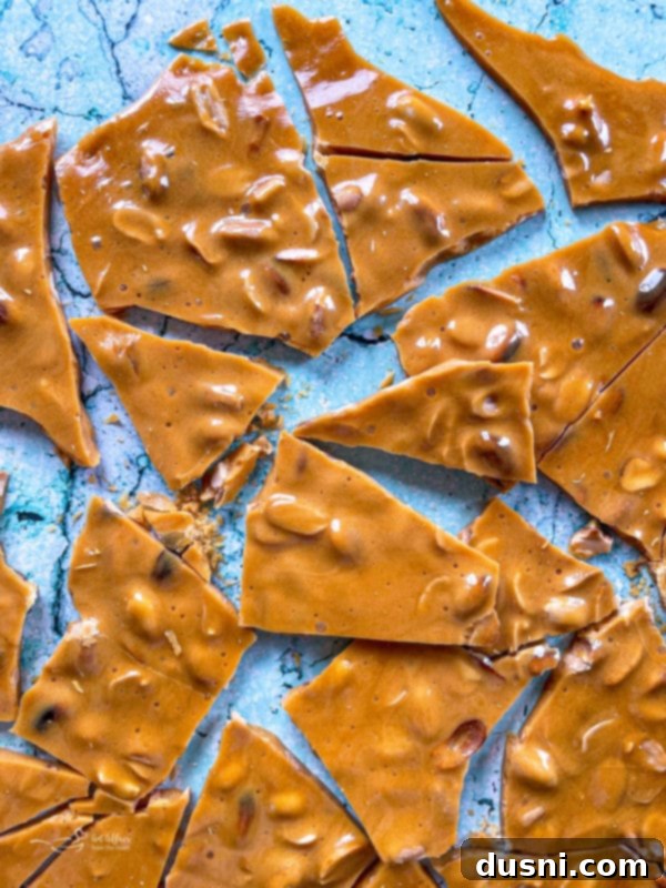 A large sheet of cooled peanut brittle cracked into pieces on a marble surface, ready for serving