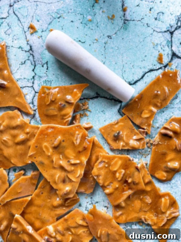 Hand breaking a piece of peanut brittle, demonstrating its crisp, shatterable texture