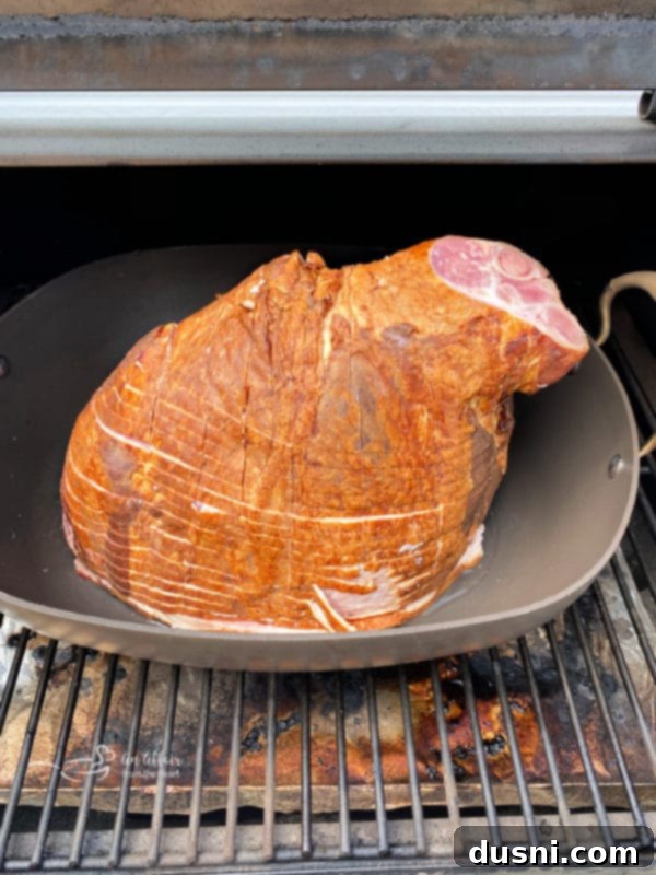 A large glazed ham cooking uncovered on an electric pellet smoker, smoke visible