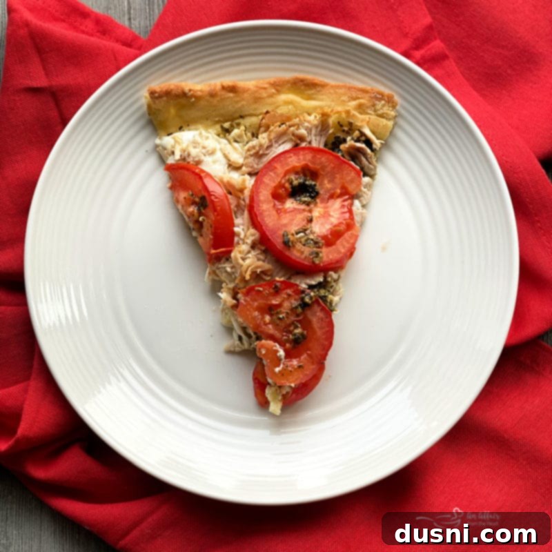 Close up view of a slice of Chicken Pesto Pizza with fresh basil garnish.