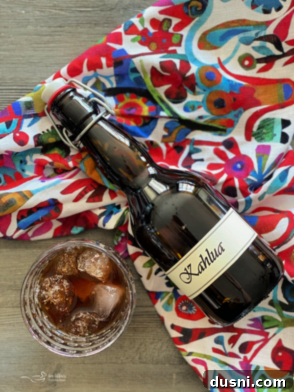 A bottle of homemade Kahlua next to a glass filled with coffee liqueur, garnished with coffee beans