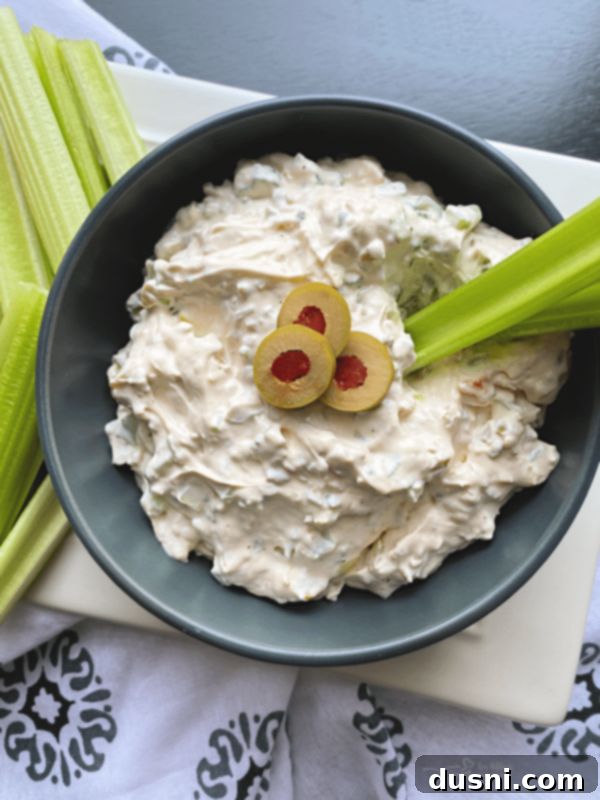 A bowl of creamy green olive dip surrounded by fresh celery sticks