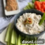 Creamy Olive Dip served with a celery stick on a white tray, surrounded by celery and carrots for dipping.
