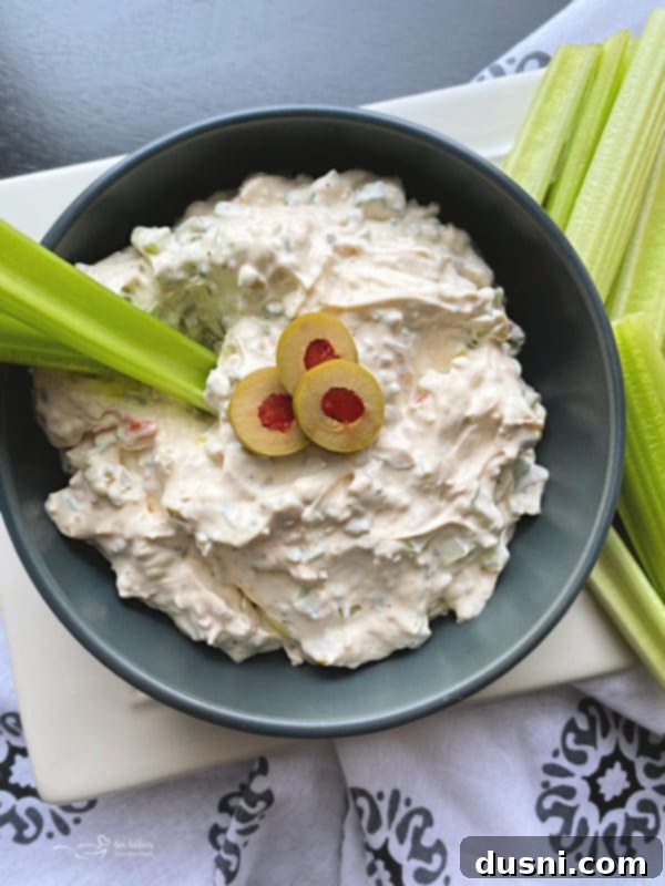 A bowl of olive dip served with an assortment of dippers, including celery, carrots, and crackers.