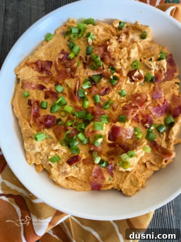 Savory Pumpkin Cheese Dip with Bacon in a white bowl, garnished with green onion and bacon bits, surrounded by crackers and celery sticks.