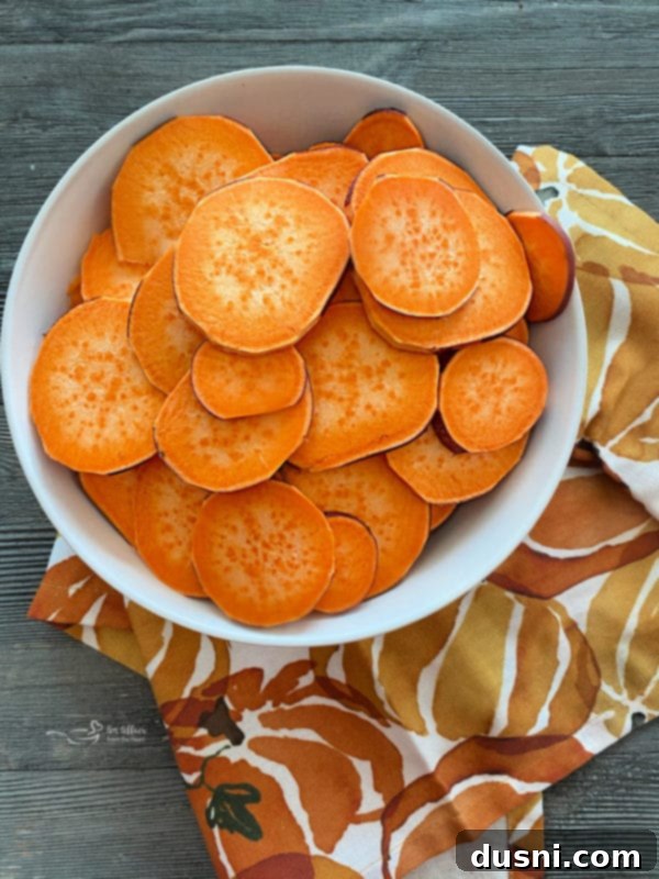 Thinly sliced sweet potatoes being prepared on a cutting board, ready for seasoning.