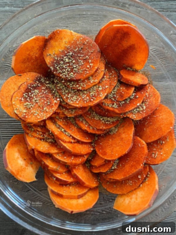 Sweet potato slices in a bowl, being sprinkled generously with paprika, seasoned salt, and oregano.