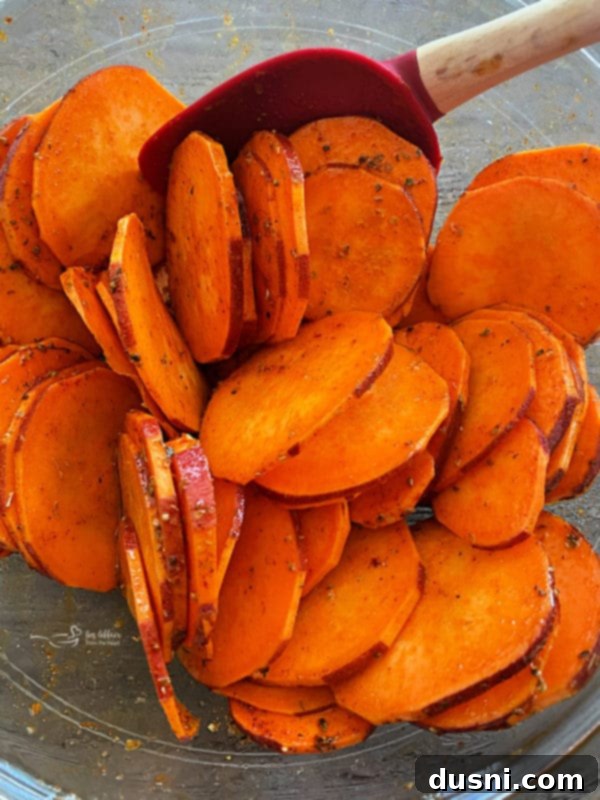 Sweet potato slices coated with olive oil and spices, being mixed in a bowl to ensure even distribution.