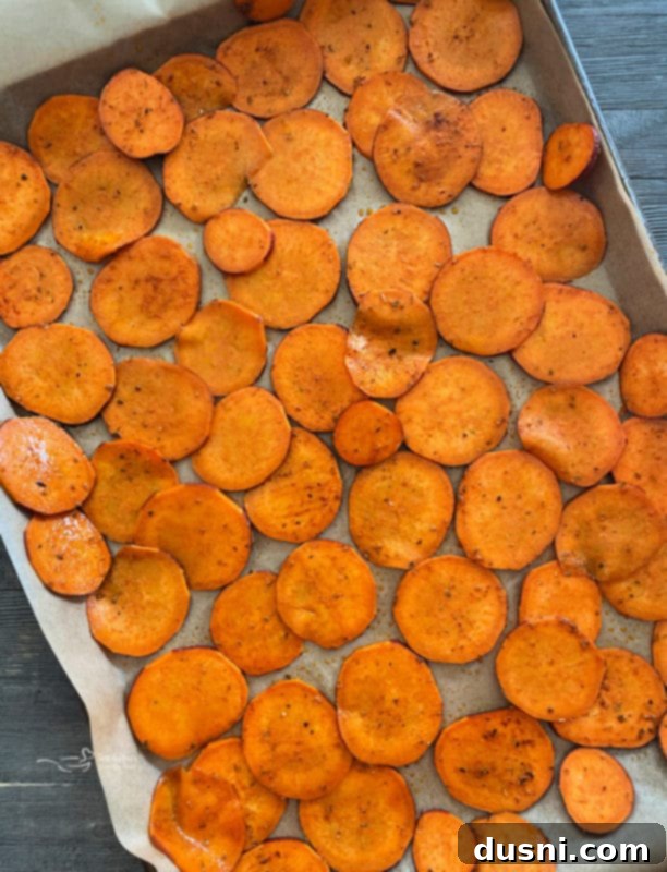 Sweet potato slices arranged in a single, even layer on a parchment-lined baking sheet, ready for the oven.