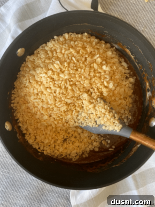 Adding Rice Krispies to the chocolate marshmallow mixture