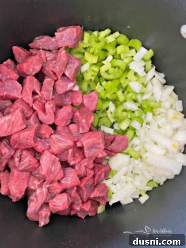 Diced beef stew meat, chopped onions, and sliced celery arranged on a cutting board, ready for the initial cooking step.