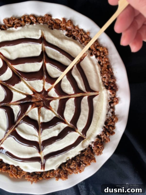 Toothpick dragging chocolate syrup to create a spider web pattern on ice cream pie