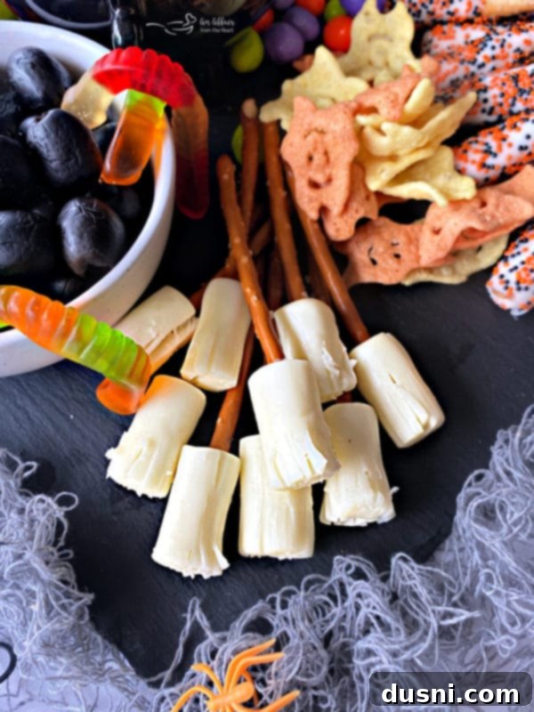 A Hauntingly Delicious Halloween Spread Sweet Savory and Peanut Butter Dip 5 Close-up image of edible witch brooms made from string cheese and pretzel sticks, arranged on a Halloween snack board.