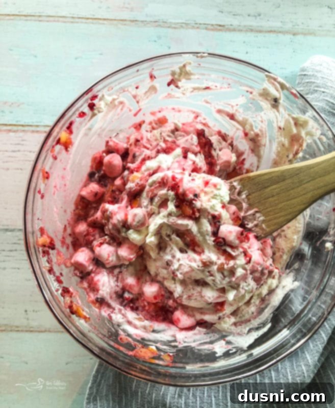 Step 4 in making Cranberry Fluff: Well-drained crushed pineapple and salt being added to the chilled cranberry and marshmallow mixture.