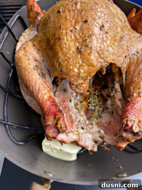 Adding a second stick of butter to the bottom of the roasting pan with the smoking turkey