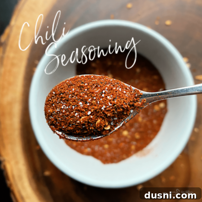 A beautiful top-down shot of a jar of homemade chili seasoning next to a small bowl of chili and fresh ingredients, showcasing culinary creativity.