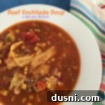 Close-up of a rustic white bowl filled with creamy Beef Enchilada Soup, topped with melted shredded cheese, for a visually appealing dish.