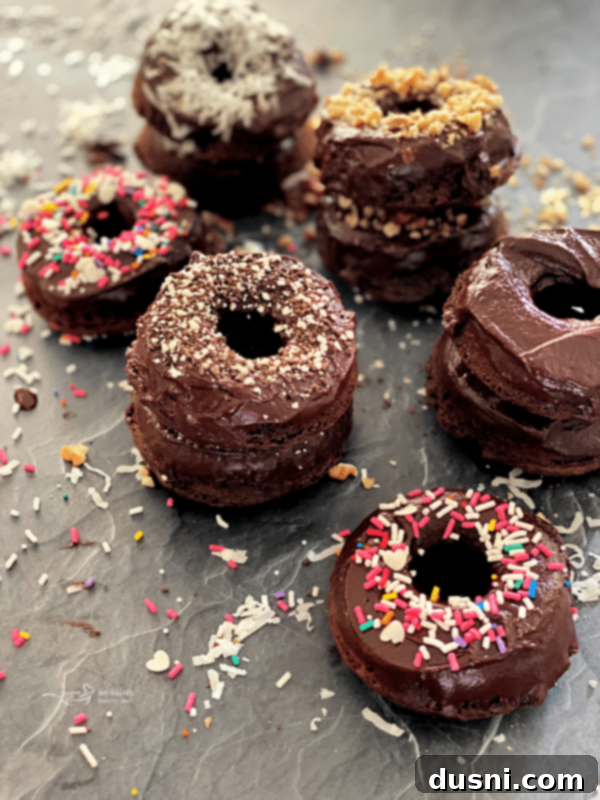 Baked Chocolate Kraut Donuts stacked on a cooling rack, glazed with chocolate ganache and decorated with sprinkles and nuts.