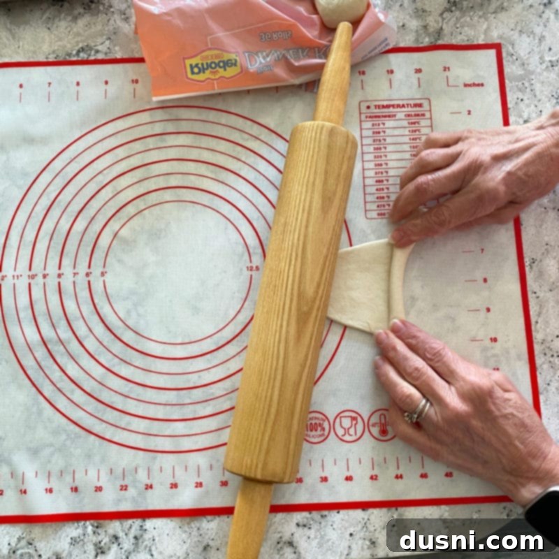 Hands demonstrating how to roll the flattened dough away from the baker.