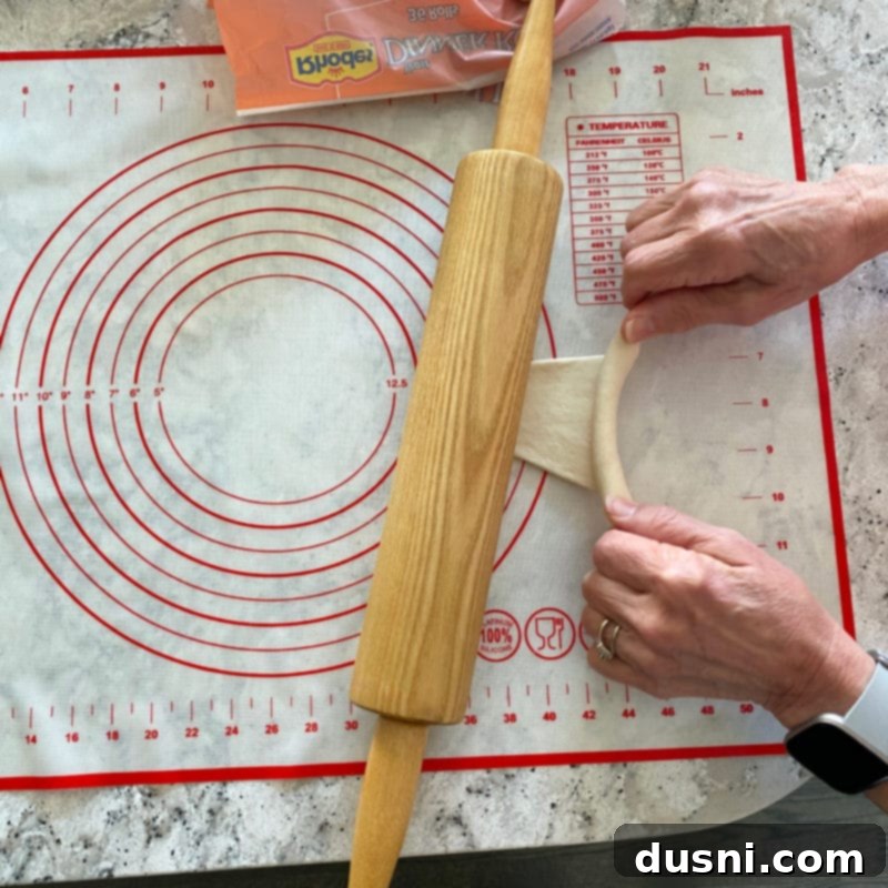 Close-up of dough being rolled, showing a slight tugging motion to stretch it.