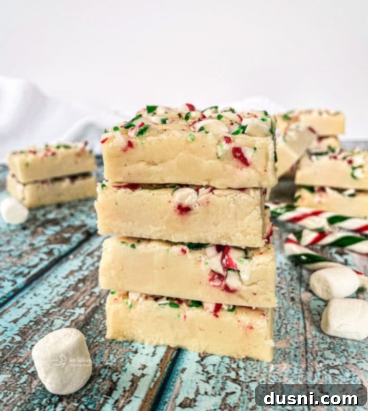 A block of homemade white chocolate peppermint fudge on a white plate, topped with crushed candy canes.