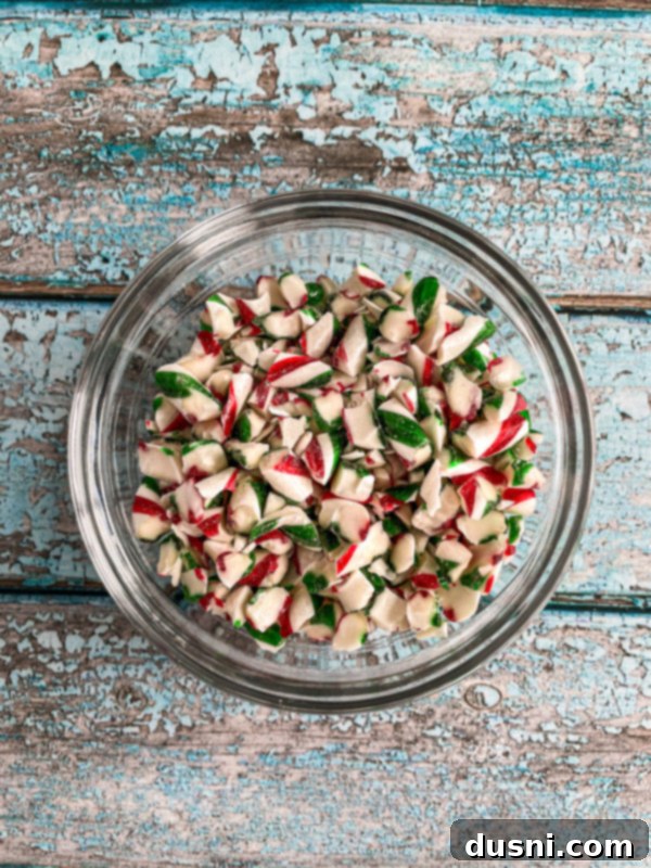 Homemade white chocolate peppermint fudge cut into squares, on a parchment-lined baking dish.