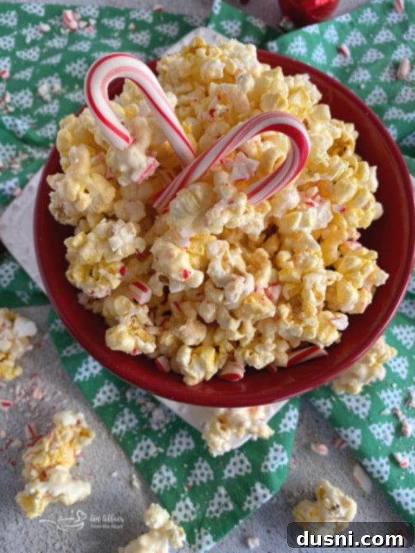 Peppermint Bark Popcorn Delight 3 A close-up shot of peppermint candy coated popcorn in a red bowl, showing the white coating and red candy cane pieces.