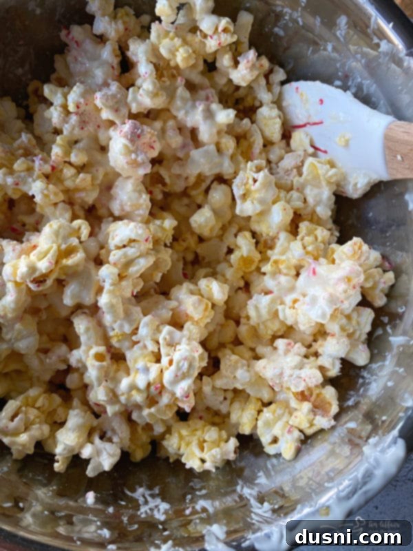 Peppermint Bark Popcorn Delight 5 Melted almond bark being poured over popped popcorn in a large bowl.