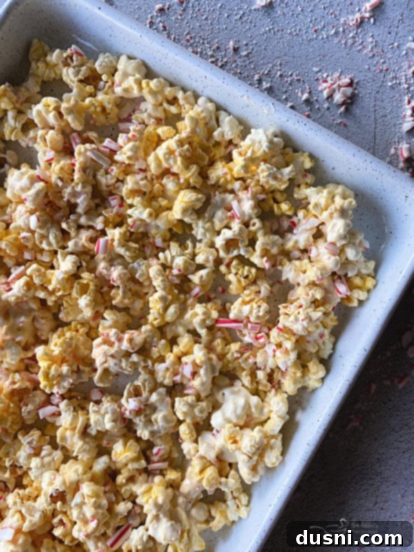 Peppermint Bark Popcorn Delight 6 Popcorn being stirred with a spatula after almond bark and crushed candy canes have been added.