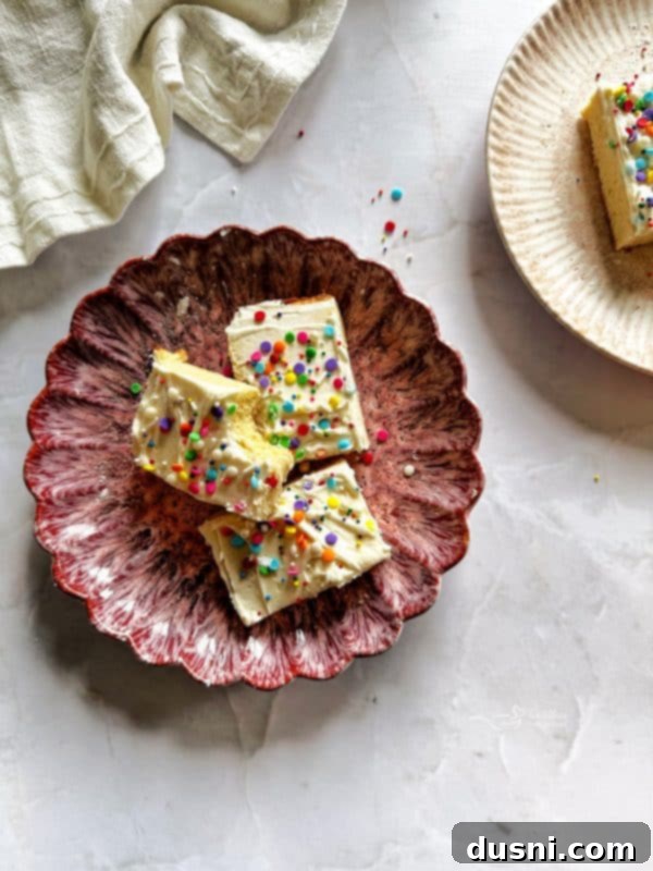 Stacked Frosted Sugar Cookie Bars on a white plate, showcasing the frosting and sprinkles.