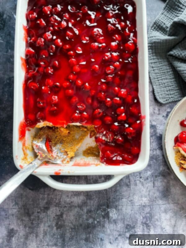 A slice of the finished cherry dessert on a plate, with a fork, emphasizing its creamy texture and rich cherry topping.