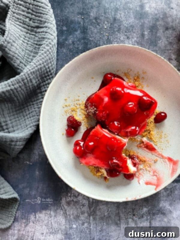 A slice of cherry dessert on a white plate, showcasing the distinct layers and garnished with a mint sprig.