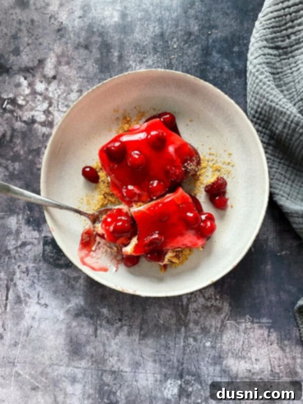 A single slice of cherry dessert with a fork, emphasizing the creamy texture and sweet-tart cherry topping.