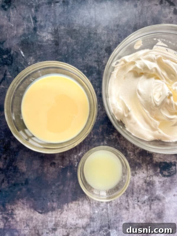 A bowl of sweetened condensed milk, a small cup of lemon juice, and a container of Cool Whip, the components for the creamy filling.