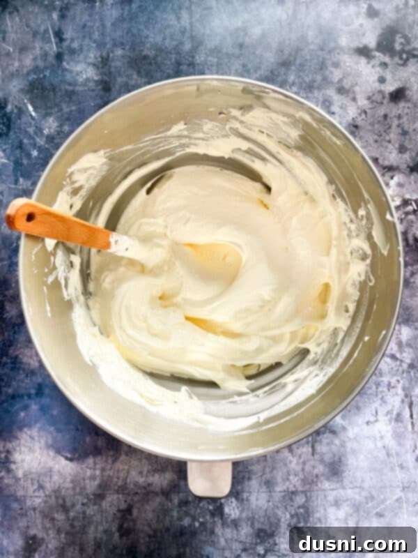 A close-up of a bowl with sweetened condensed milk and lemon juice being mixed with an electric hand mixer, showing the mixture beginning to thicken.