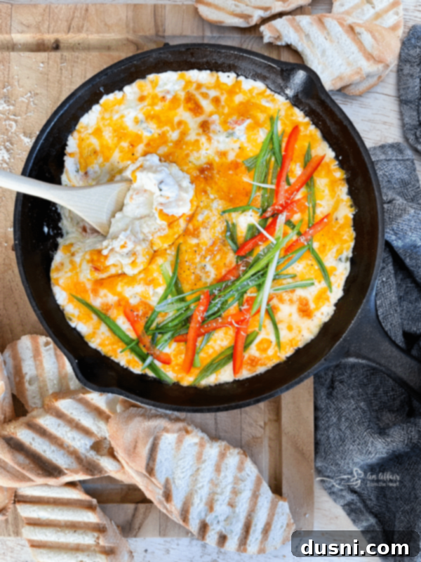 A close-up shot of creamy slow cooker crab dip garnished with green onions and red peppers, served with toasted bread slices.