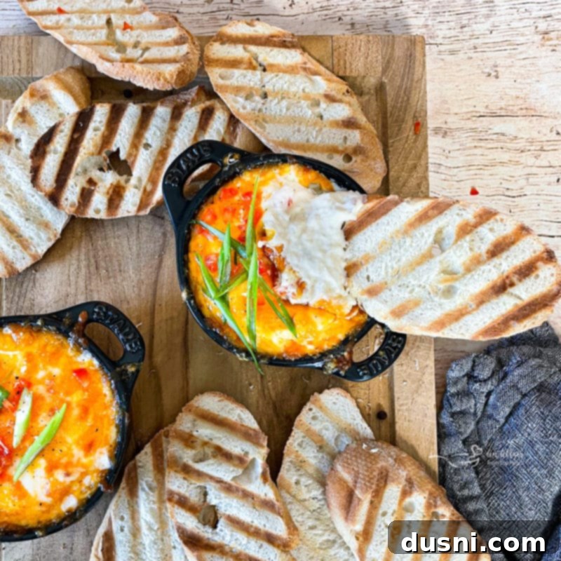 Slow Cooker Crab Dip served in individual Staub mini cocottes with small spoons, set on a wooden table.