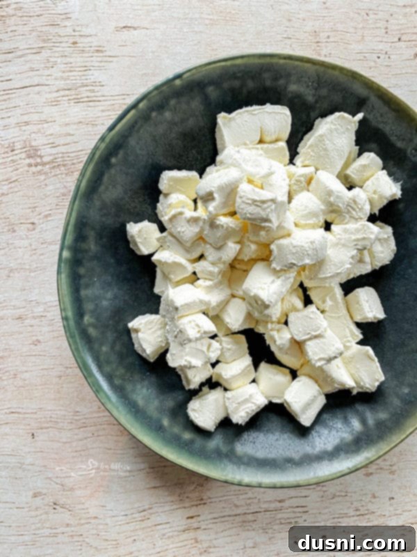 Cubed cream cheese and other ingredients in a slow cooker, ready to be cooked for the crab dip.