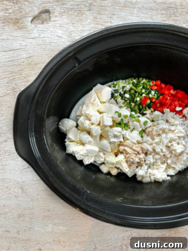 Slow Cooker Crab Dip in a crockpot, served with toasted baguettes and garnished with green onions and red peppers.