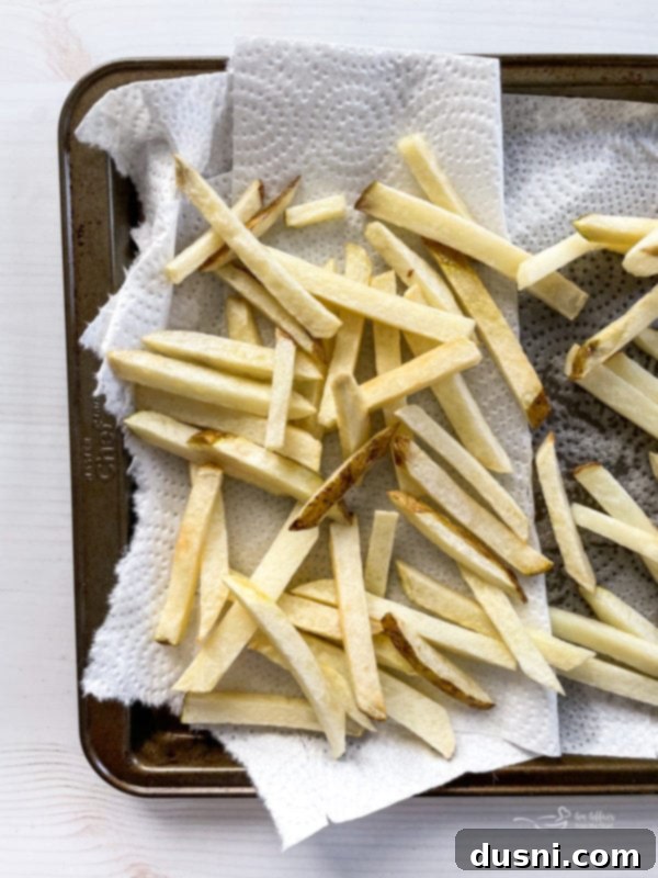 Sliced potatoes on baking sheet with parchment paper, prepared for frying.